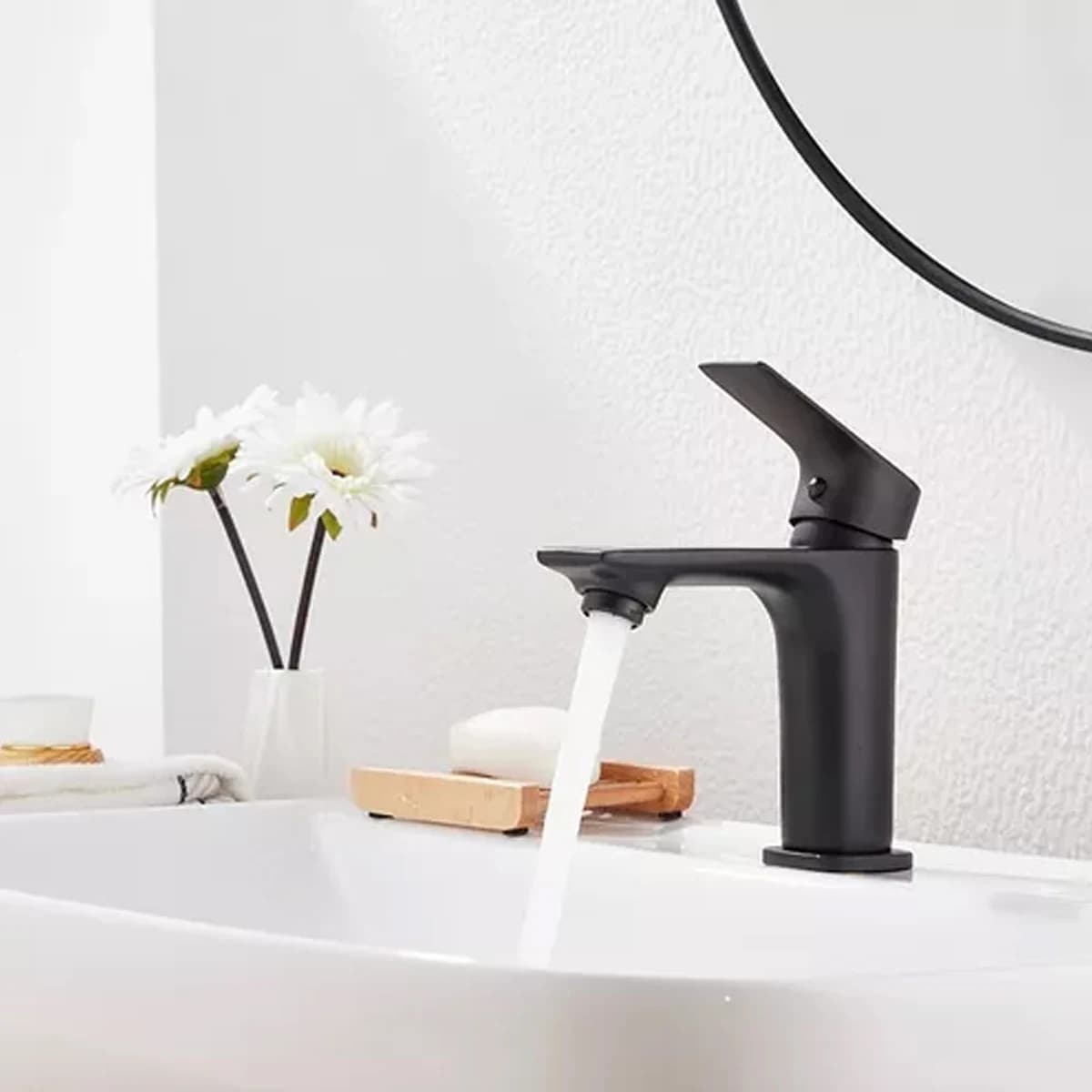 Torneira monocomando preta para lavatório de banheiro, design elegante, fundo branco, água fluindo.