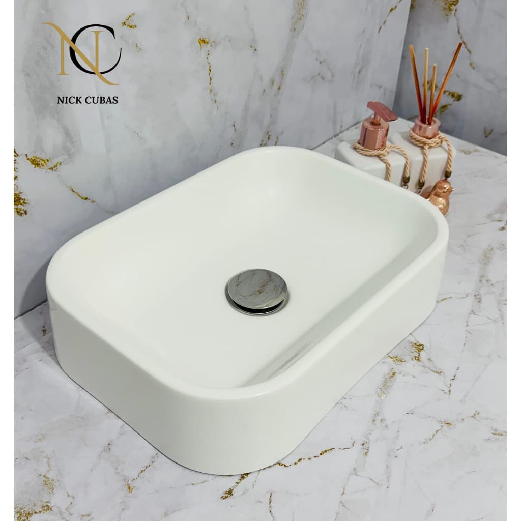 Cuba de cerâmica oval branca com válvula cromada em fundo de mármore