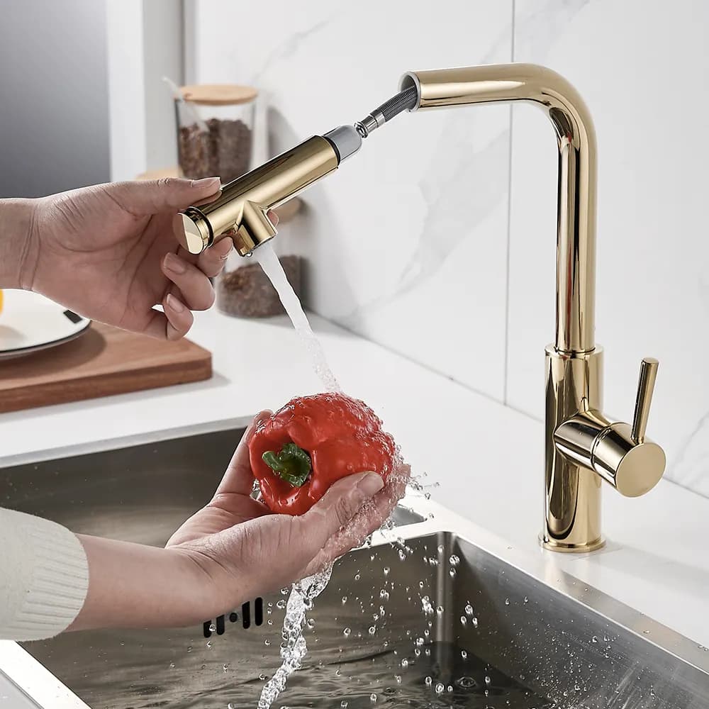 Torneira de cozinha em aço inoxidável dourado com bico pulverizador, água fluindo e pimentão vermelho na mão